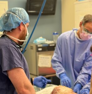 Two surgeons in an operating room. The room is filled with monitors, cables, and advanced medical devices.
