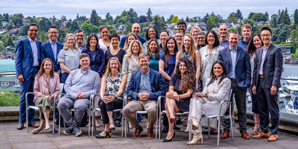 Group portrait of approximately 30 employees seated and standing on an outdoor terrace overlooking a waterfront neighborhood.